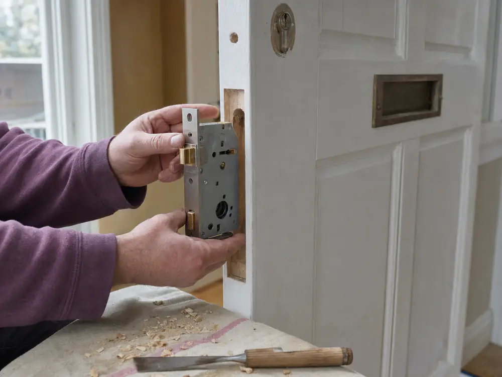 Slotenmaker plaatst een nieuw insteekslot in de kant van een houten deur